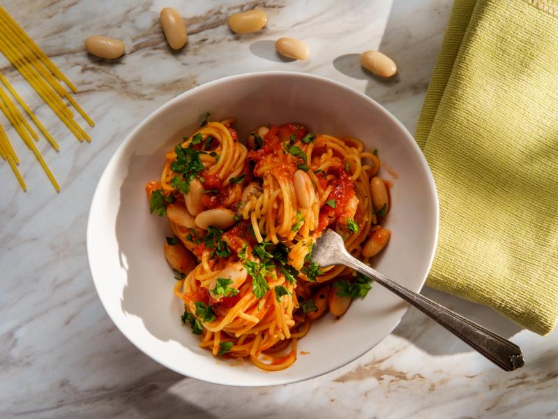 Bowl of spaghetti in marinera sauce with white beans and parsley.