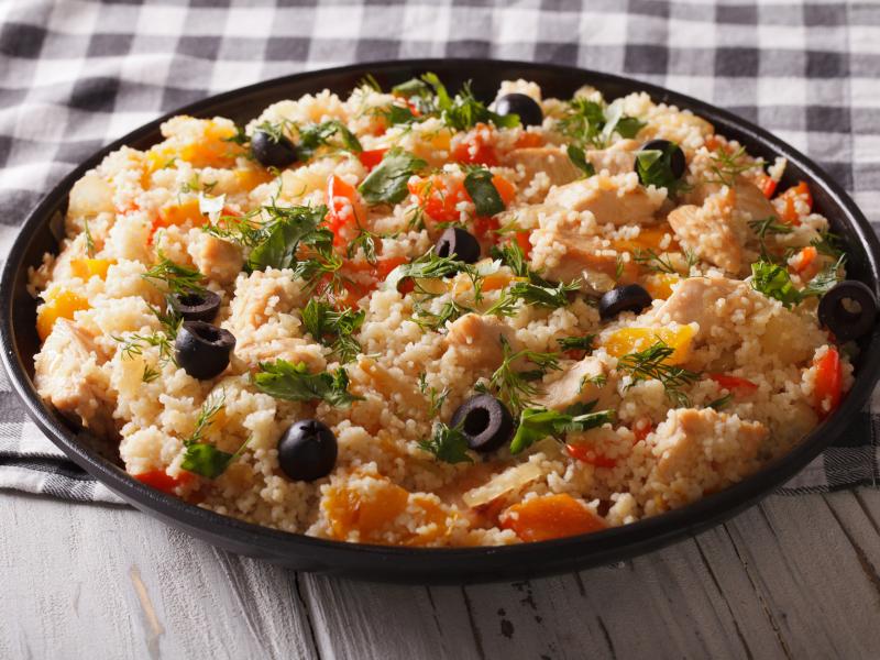 Bowl of couscous with canned tuna, olives, walnuts, and peppercinis.