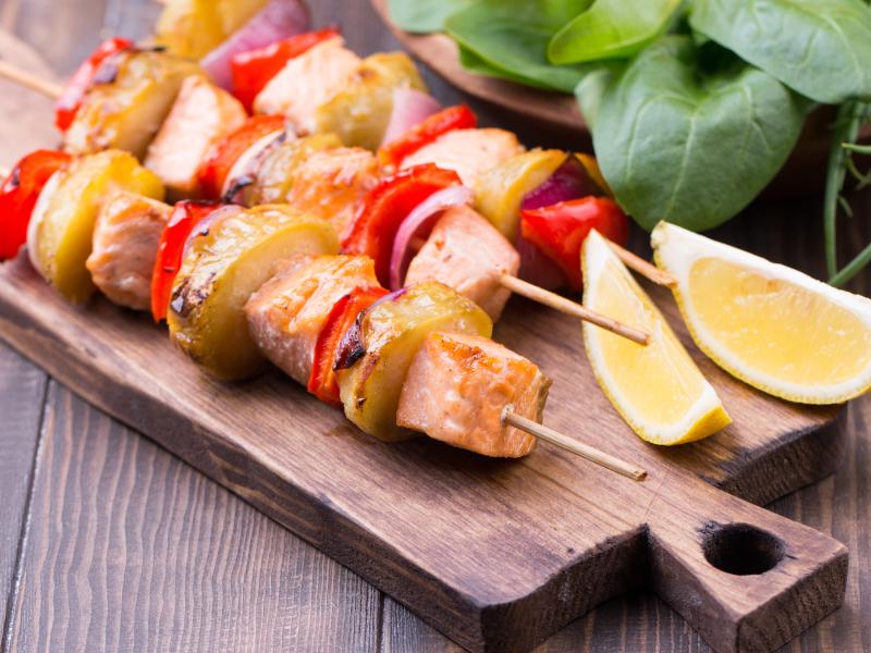 Cut up skewered salmon and vegetables on a cutting board.