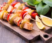 Cut up skewered salmon and vegetables on a cutting board.