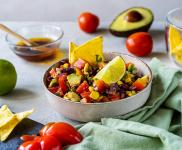 Bowl of Cowboy Caviar on a table alongside chips and vegetables